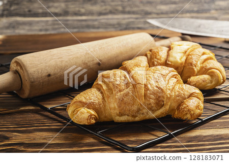 Freshly baked croissants on a cooling tray with a rolling pin on the table 128183071