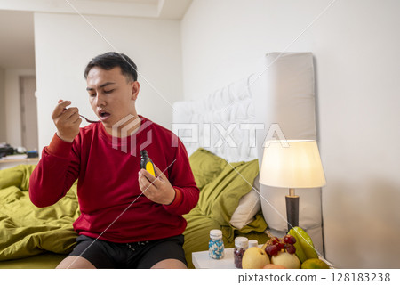 Indonesian southeast asian man sitting on the bed at home gets medicine for coughing. Suffer from fever, flu, and cold. Healthcare and medical concept 128183238