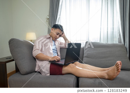 Indonesian southeast asian man with his laptop, unhappy and feeling sad, depressed, and anxious in his house. Stressed, tired, and overworked. Healthcare concept 128183249