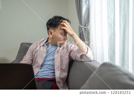 Indonesian southeast asian man with his laptop, unhappy and feeling sad, depressed, and anxious in his house. Stressed, tired, and overworked. Healthcare concept 128183251