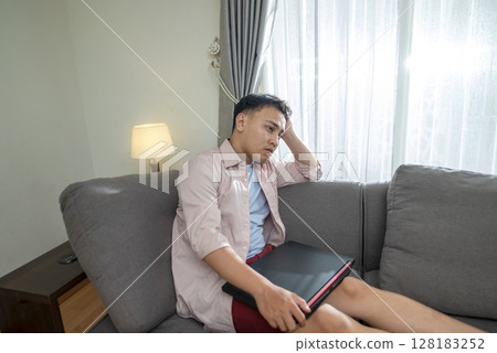 Indonesian southeast asian man with his laptop, unhappy and feeling sad, depressed, and anxious in his house. Stressed, tired, and overworked. Healthcare concept 128183252