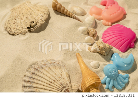 Seashells and beach toys on a beautiful sandy beach. Natural background. Summer concept. Top view Seashells and beach toys on a beautiful sandy beach. Natural background. Summer concept. Top view 128183331