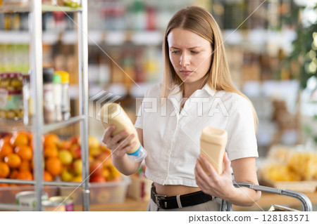 Choose food in supermarket - woman chooses mayonnaise to buy in the grocery department section of store Choose food in supermarket - woman chooses mayonnaise to buy in the grocery department section of store 128183571