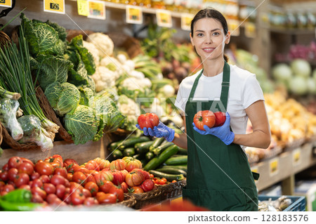 Girl shop seller add tomato goods on display case in vegetable store 128183576