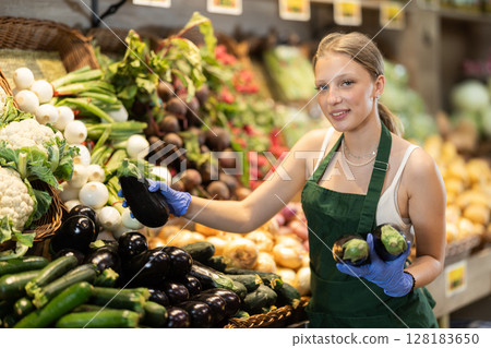Young woman seller putting eggplants in vegetable shop 128183650