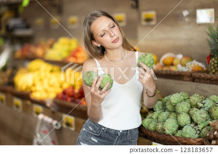 Young woman choosing artichoke in vegetable shop Young woman choosing artichoke in vegetable shop 128183657