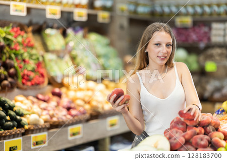 Focused woman shopping in organic food store, choosing flat peaches 128183700