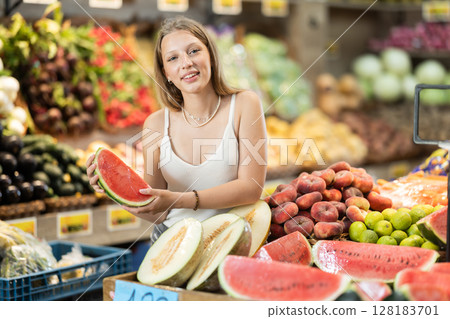 blonde woman standing in a fruit shop and choosing a ripe watermelon 128183701