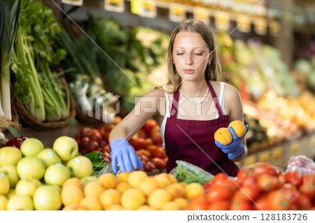 Working in supermarket - female salesman sorts through ripe peaches on display case Working in supermarket - female salesman sorts through ripe peaches on display case 128183726