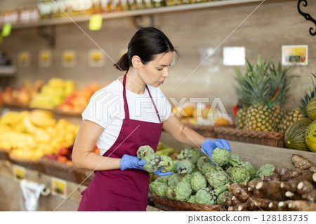 saleswoman lays out artichokes on a shelf in a store 128183735