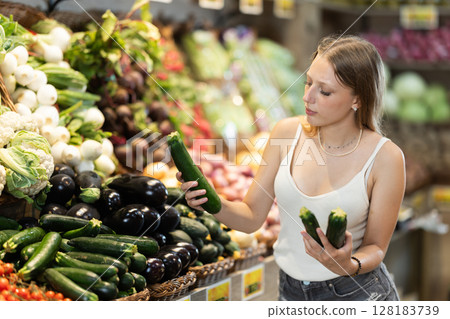 Portrait of female shopper carefully selecting eggplants in supermarket 128183739
