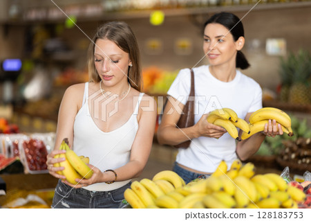 Two women are standing near the counter and choosing bananas Two women are standing near the counter and choosing bananas 128183753