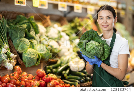 Adult woman seller puts cabbage in vegetable shop 128183764