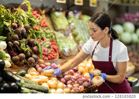 Woman seller putting onions on display case 128183820