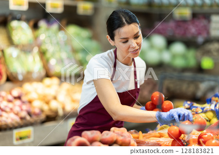 Adult woman seller puts tomatoes in vegetable shop 128183821
