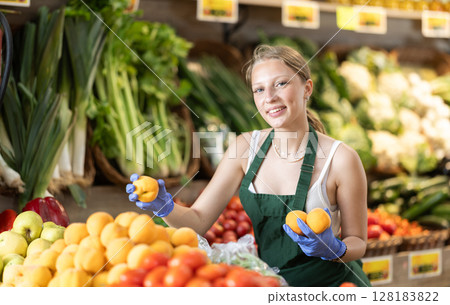 Working in supermarket - female salesman sorts through ripe peaches on display case 128183822