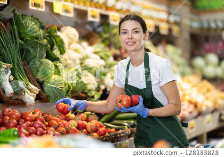 Girl shop seller add tomato goods on display case in vegetable store 128183828
