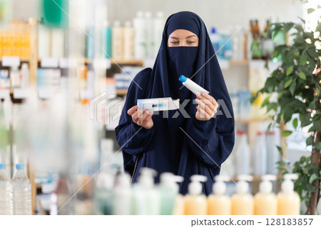 Female customer in Muslim attire choosing ointment in pharmacy 128183857