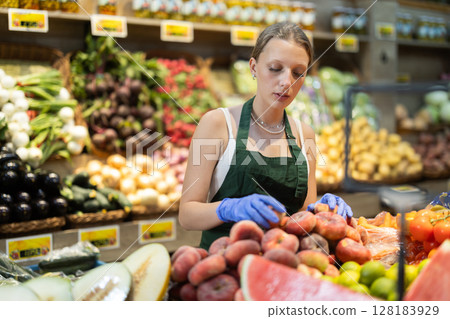Young woman seller puts flat peaches in vegetable shop 128183929
