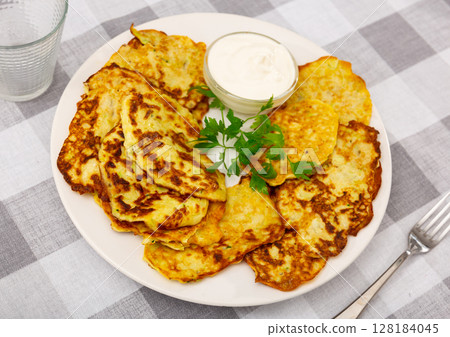 Zucchini pancakes served with sour cream 128184045