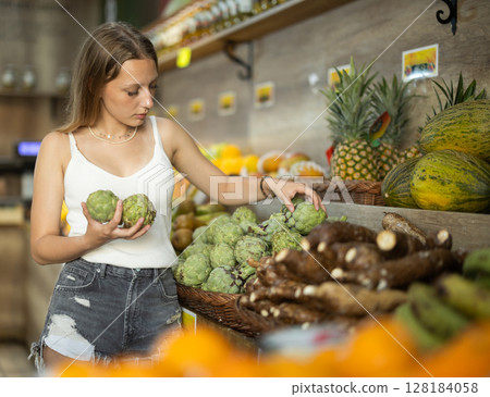 Young woman choosing artichokes in a shop Young woman choosing artichokes in a shop 128184058