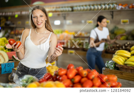 Young woman standing in store and holding tomatoes 128184092