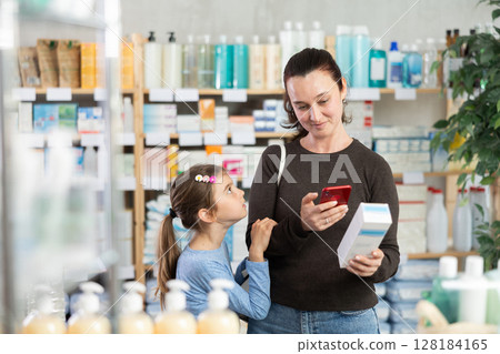 Woman with daughter in pharmacy scans QR code on cream 128184165
