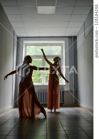 Silhouette of two dancers performing graceful artistic moves with their hands in corridor Silhouette of two dancers performing graceful artistic moves with their hands in corridor 128184288