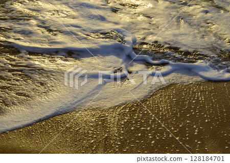 Morning light bathes the beach north of Cairns, Queensland, Australia, illuminating the Coral Sea with soft hues and tranquil reflections, capturing the calm beauty of a tropical coastal sunrise. 128184701