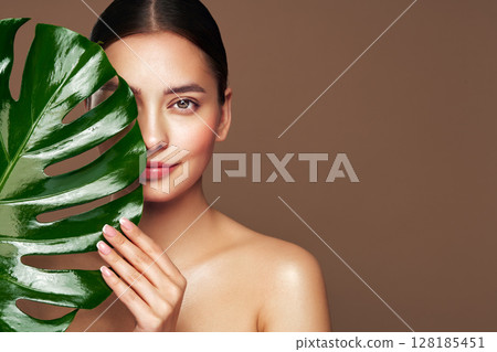 Close up woman face with green exotic leaf Close up woman face with green exotic leaf 128185451