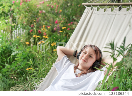 Teenage girl relaxing in hammock listening to music in garden 128186244