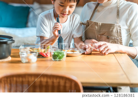 Family enjoying cooking together, preparing meals and serving curry at a cottage (family trip/glamping) 128186381