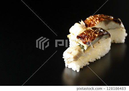 Grilled mackerel sushi photographed against a black background 128186483