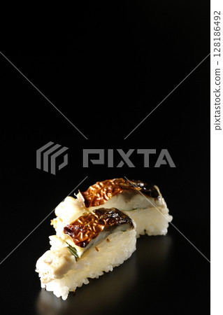 Grilled mackerel sushi photographed against a black background 128186492