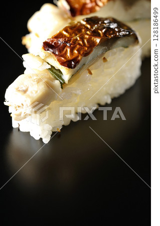 Grilled mackerel sushi photographed against a black background 128186499