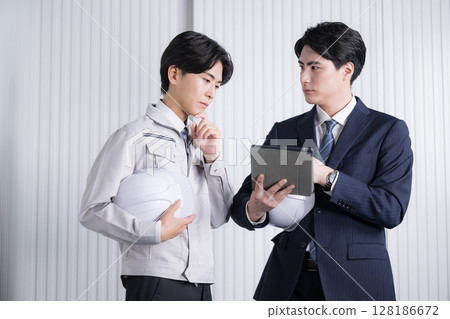 一名身穿工作服和西裝的男子在總承包商的現場等處檢查文件。在會議上檢查文件 128186672