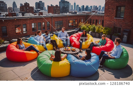 Group of people are sitting on colorful bean bags on a rooftop. Scene is relaxed and social, as the group of people are gathered together to enjoy each other's company. The colorful bean bags add a 128186740