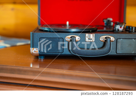Open vintage record player in suitcase design with vinyl lying nearby. Retro music setup ready for playback in warm, nostalgic atmosphere. 128187293