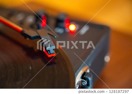 Close-up of record player needle tracking vinyl grooves during playback. Analog sound detail capturing retro music atmosphere. 128187297
