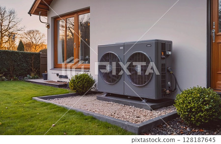 Gray and black air conditioner is outside of a house. The air conditioner is on the side of a house and is surrounded by a gravel area 128187645
