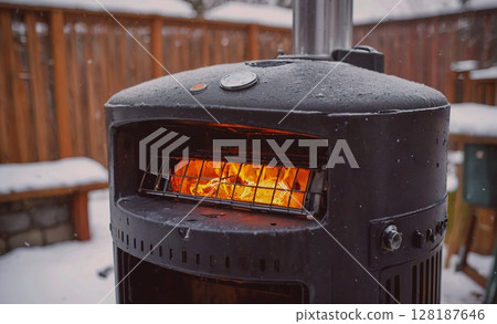 Black outdoor heater with a fire burning inside. The fire is warm and inviting, and the heater is surrounded by snow 128187646