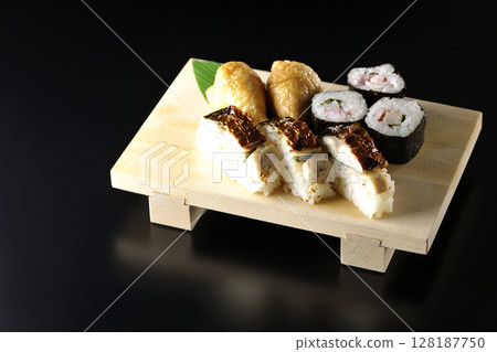 Grilled mackerel, norimaki, and inari sushi photographed against a black background 128187750