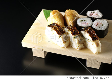 Grilled mackerel, norimaki, and inari sushi photographed against a black background 128187756