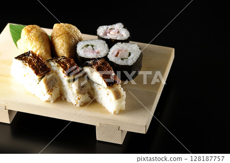 Grilled mackerel, norimaki, and inari sushi photographed against a black background 128187757