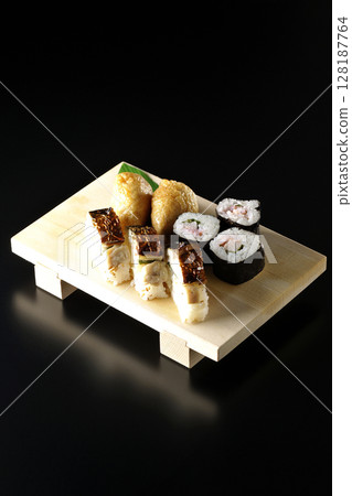 Grilled mackerel, norimaki, and inari sushi photographed against a black background 128187764