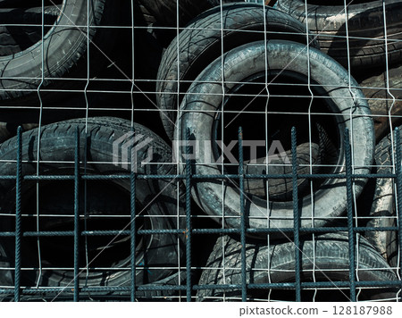 A Stack of Used Tires Behind a Metal Fence in Direct Sunlight A Stack of Used Tires Behind a Metal Fence in Direct Sunlight 128187988