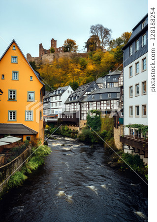 Historic Buildings Along a River With Autumn Foliage and Ruins in the Background in a Quaint Village 128188254
