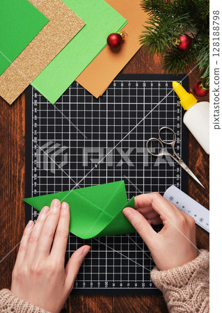 Let's make a simple paper craft. A Christmas tree bookmark. Hands fold the paper. Let's make a simple paper craft. A Christmas tree bookmark. Hands fold the paper. 128188798