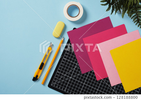 Workspace for paper crafts. Black cutting mat, colored paper, pencils, craft knife, ruler, tape. Blue background. Space for your text. 128188800