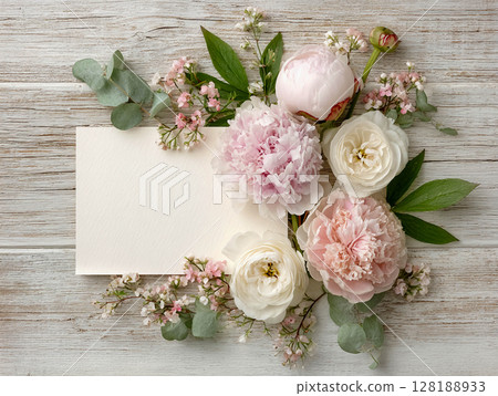 A composition of various flower bouquets arranged around a white blank sheet or card lying on a wooden surface. Suitable for congratulations, invitations, or decorative purposes. 128188933